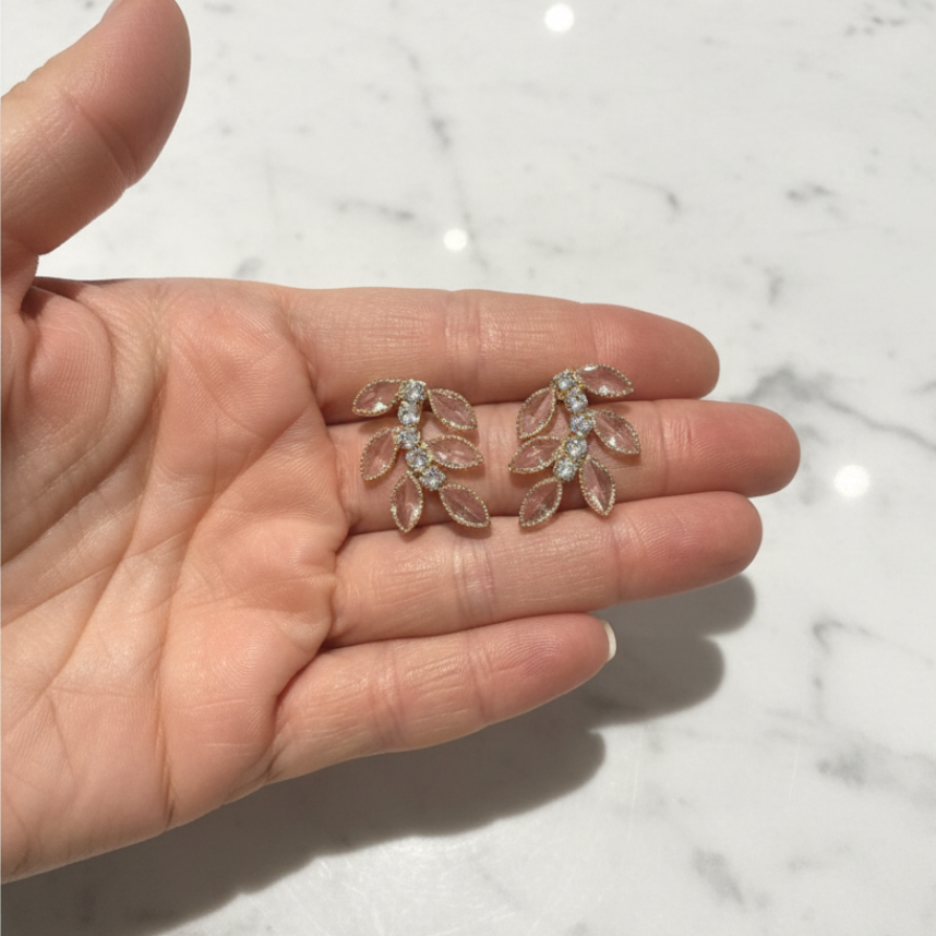 elephantina.gr gold leaf-shaped stud earrings with clear marquise-cut crystals held in a palm