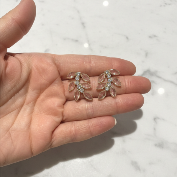 elephantina.gr gold leaf-shaped stud earrings with clear marquise-cut crystals held in a palm