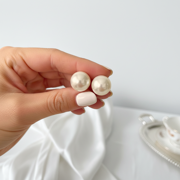 elephantina.gr Θύμιο pearl stud earrings held between fingers against a white silk background