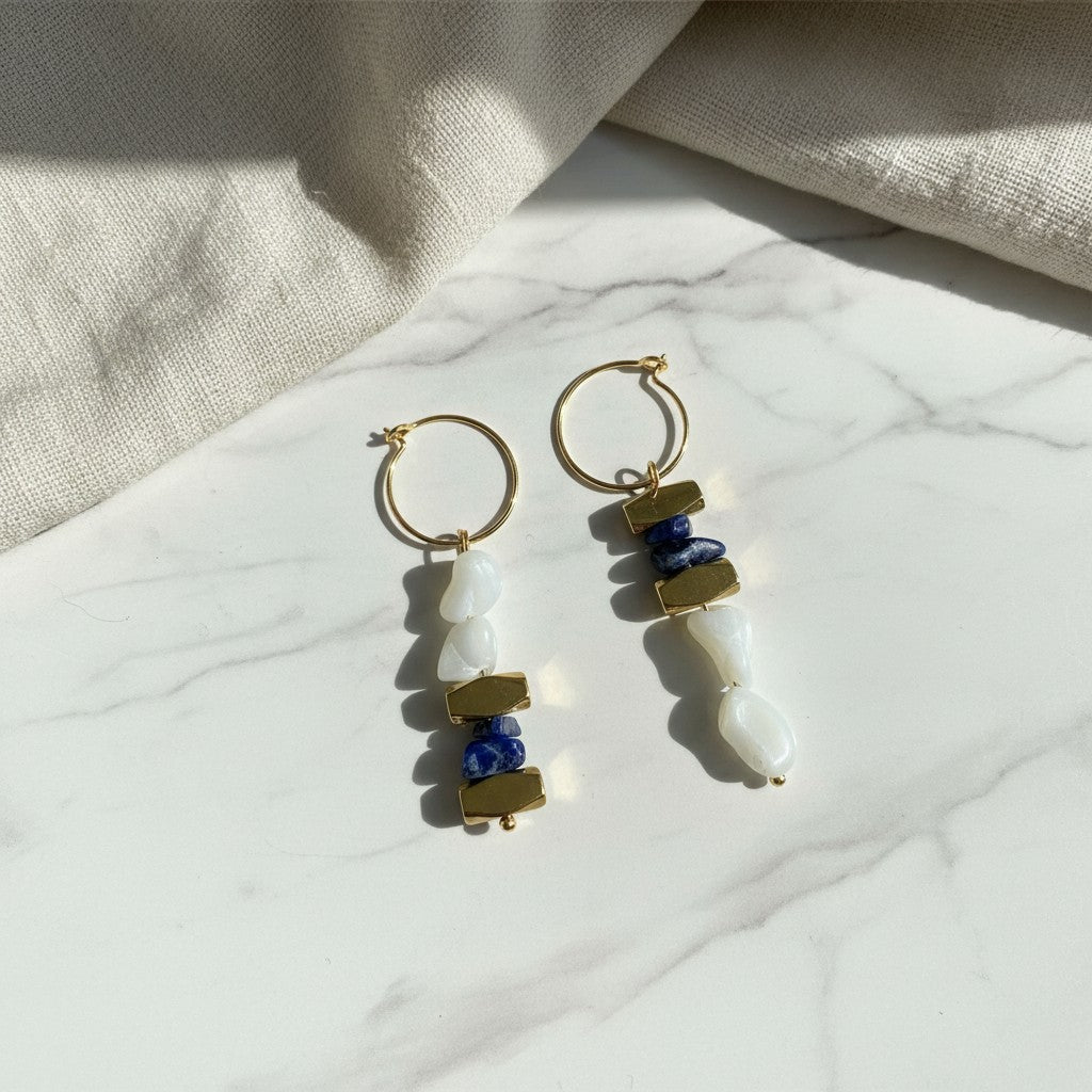 elephantina.gr gold hoop earrings featuring dangling blue lapis lazuli and white shell beads on a marble surface
