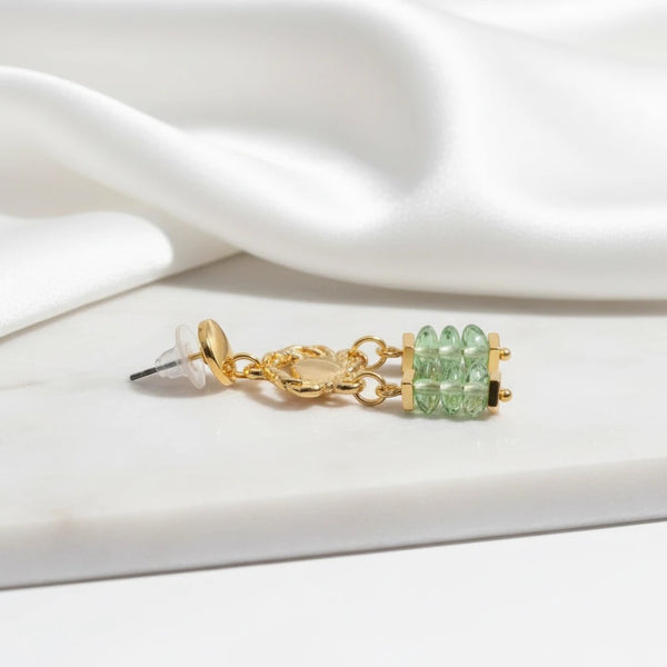 elephantina.gr gold-plated stud earrings featuring a crab charm and green glass beads on a white silk background.