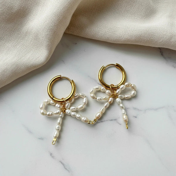 elephantina.gr gold-plated hoop earrings with handmade rice pearl bow charms on a marble surface.