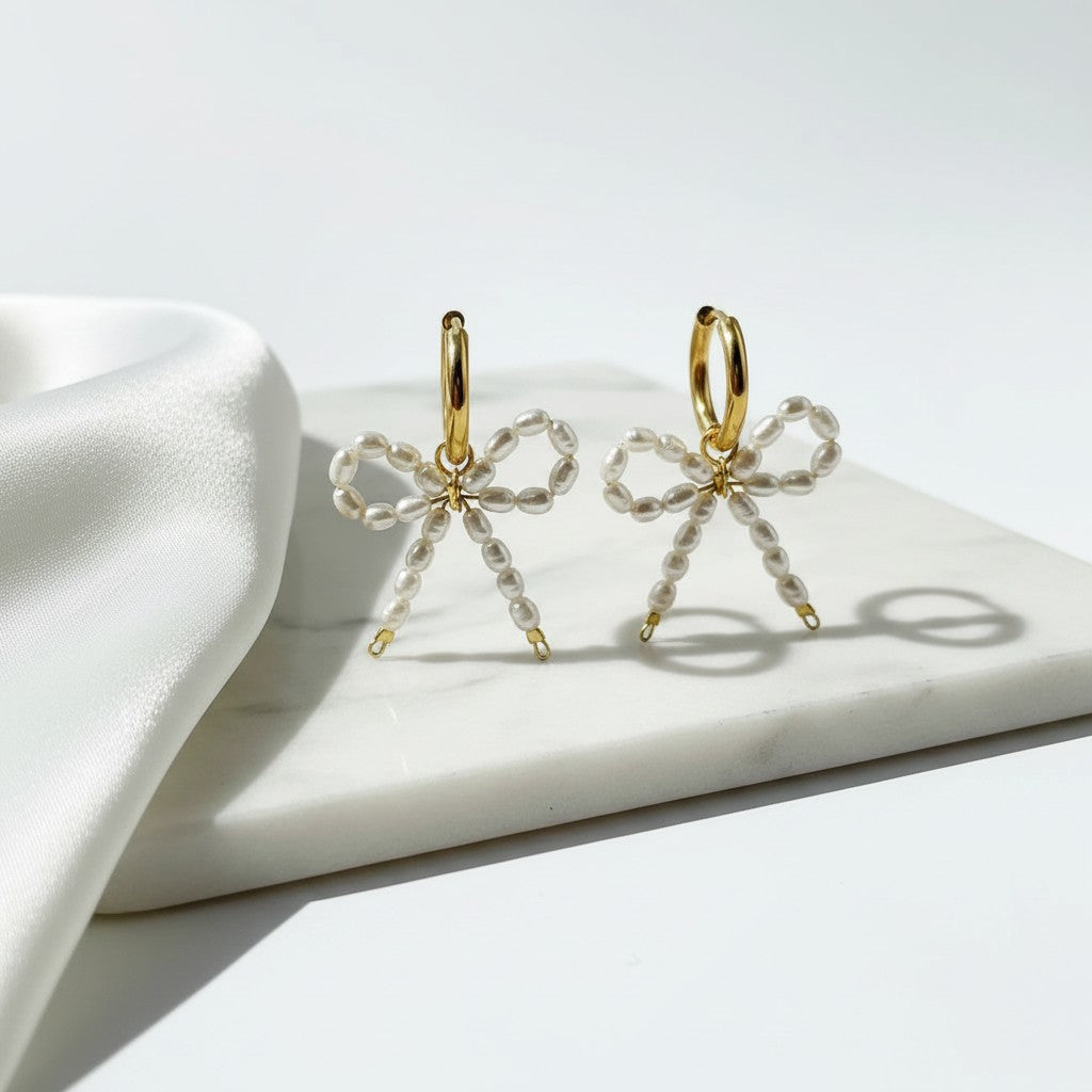 elephantina.gr gold-plated hoop earrings with romantic white rice pearl bow charms on a marble surface.