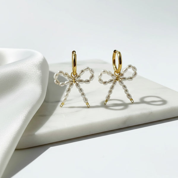 elephantina.gr gold-plated hoop earrings with romantic white rice pearl bow charms on a marble surface.