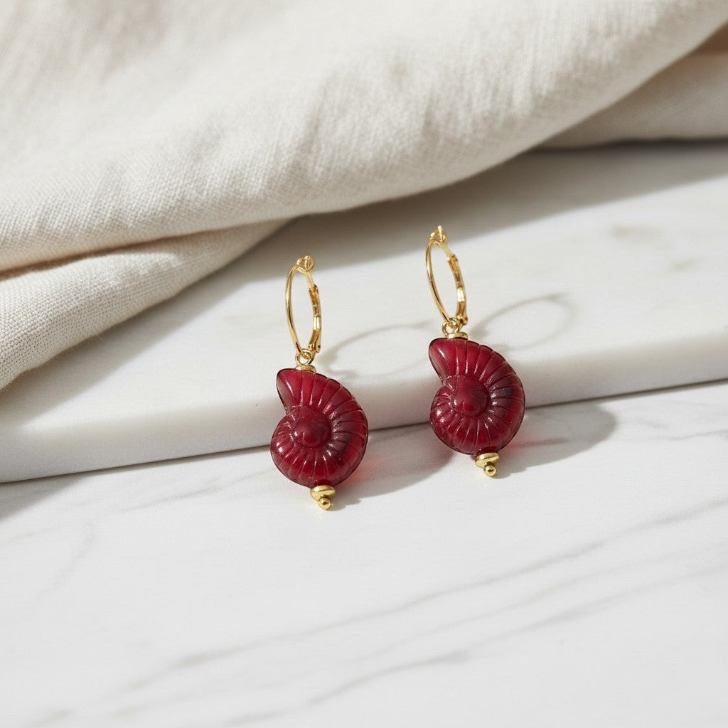 elephantina.gr gold hoop earrings featuring carved deep red ammonite shell pendants on a marble surface