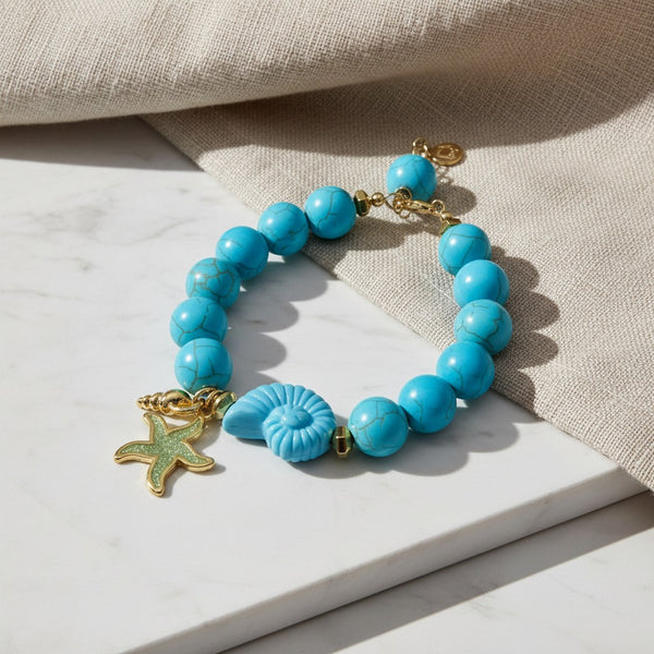 elephantina.gr HHy bracelet featuring turquoise beads, a gold starfish charm, and a seashell accent on marble
