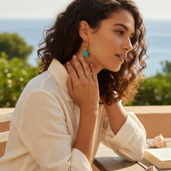 elephantina.gr gold hoop earring with a turquoise starfish charm worn by a woman outdoors by the sea