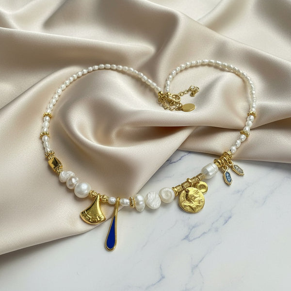 Elephantina.gr pearl and gold charm necklace with navy blue drop, ancient Greek trumpet, coin, and enamel charms.