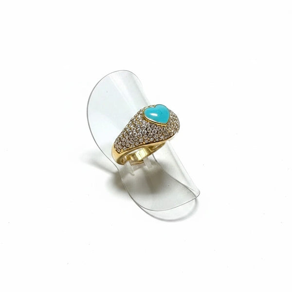 elephantina.gr gold-tone statement ring with a turquoise heart centerpiece and pavé crystal band on a clear stand.