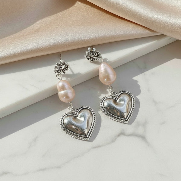 elephantina.gr silver-plated brass heart earrings with baroque pearls and eye-shaped studs on a marble surface.