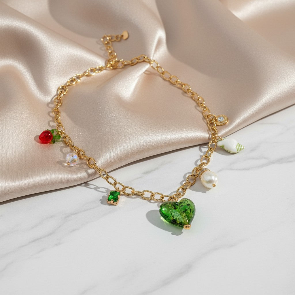 Gold chain necklace with a green Murano glass heart, pearl, strawberry, seashell, and crystal charms. elephantina.gr