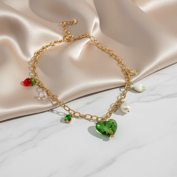 Gold chain necklace with a green Murano glass heart, pearl, strawberry, seashell, and crystal charms. elephantina.gr