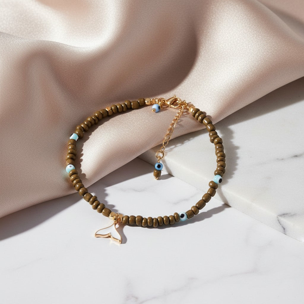 elephantina.gr anklet with olive beads, blue evil eye charms, and a white enamel whale tail pendant.