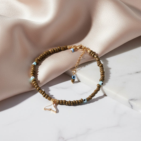 elephantina.gr anklet with olive beads, blue evil eye charms, and a white enamel whale tail pendant.
