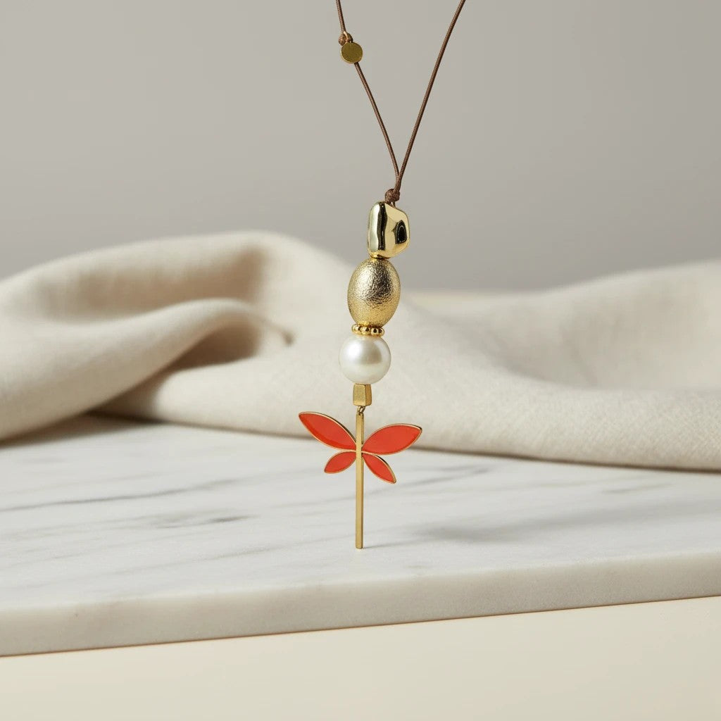 Elephantina.gr long necklace with black cord, pearl, gold beads and coral enamel dragonfly pendant.