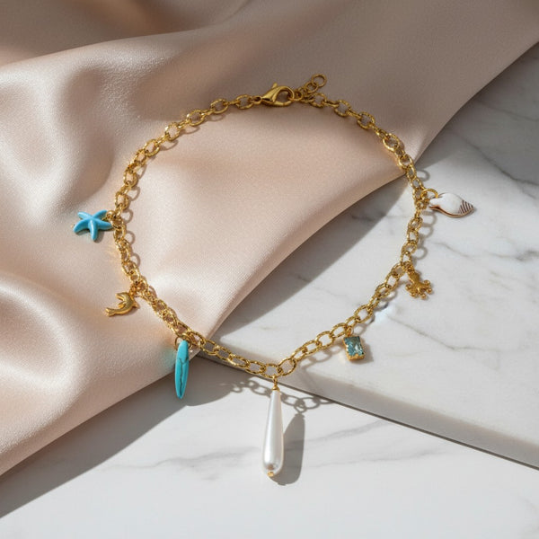 Gold chain necklace with sea charms: pearl drop, starfish, shell, dolphin, octopus, surf board, and blue stone. elephantina.gr