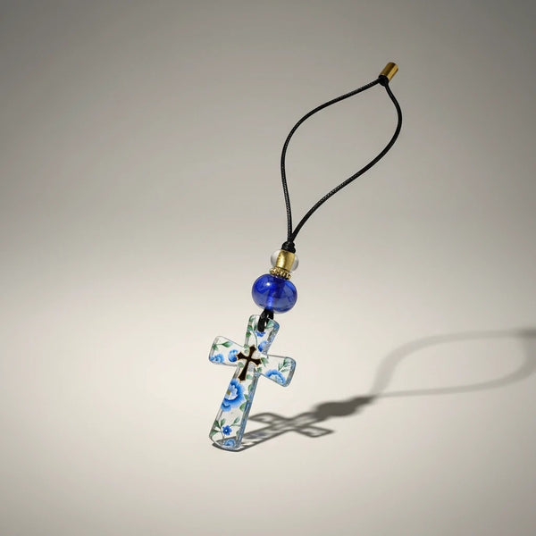 Clear glass cross pendant with blue floral design, black cord, blue bead, and gold accent. elephantina.gr