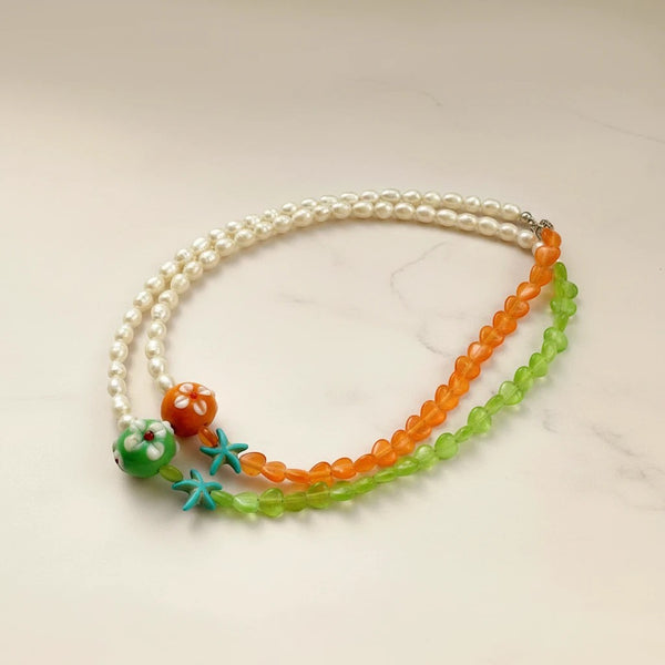Handmade elephantina.gr necklace with white pearls, orange and green heart beads, and starfish charms.