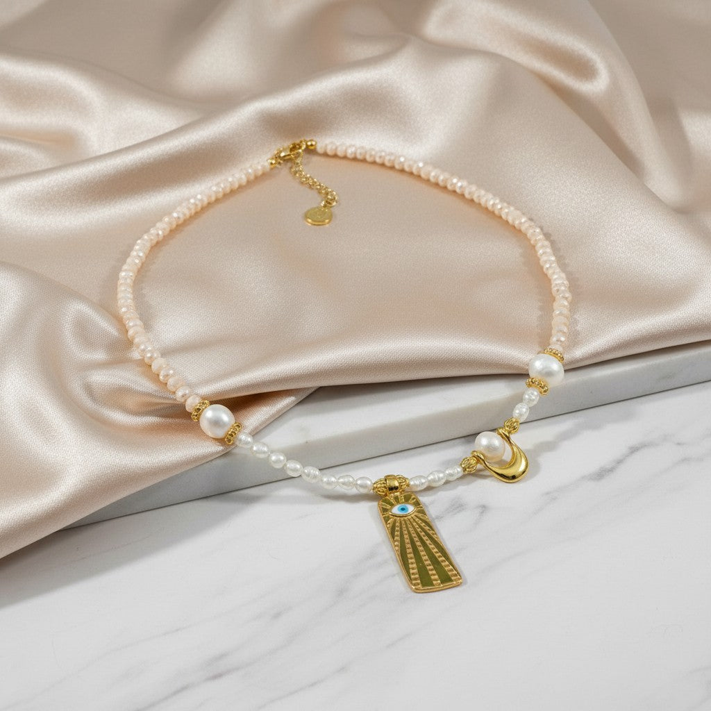 elephantina.gr gold necklace with pearls, nude crystals, sun motif with blue eye, and crescent charm.