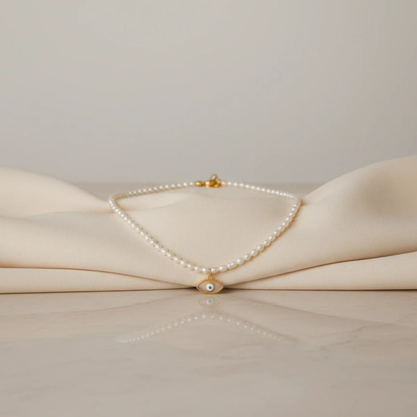 elephantina.gr necklace with small white pearls and a gold evil eye charm with blue detail. Minimalist and elegant.