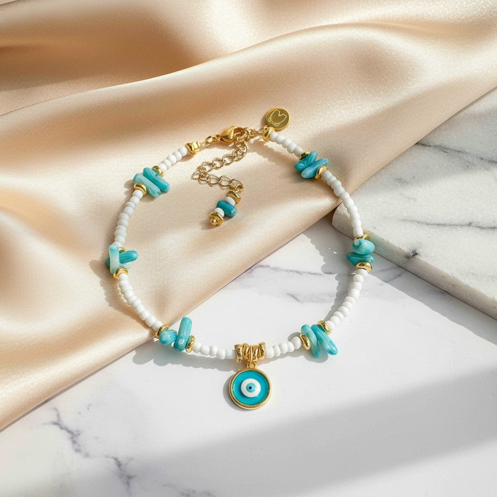 Elephantina.gr white beaded anklet with turquoise chips, blue coral beads, and a gold evil eye charm.