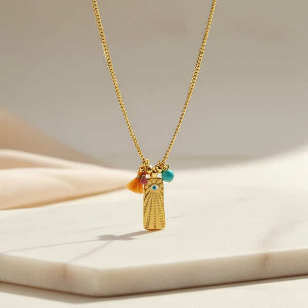 Gold plated stainless steel chain necklace with rectangular ID tag featuring an evil eye design, tassels, and a turquoise bead.