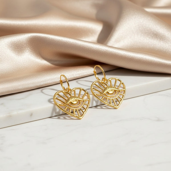 elephantina.gr gold-tone brass hoop earrings featuring heart-shaped charms with an evil eye design.