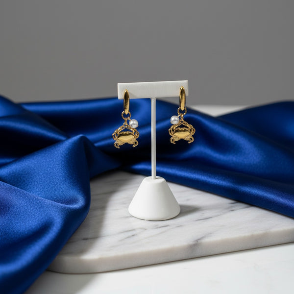 Gold-tone dangle earrings featuring crab charms with pearl accents. elephantina.gr