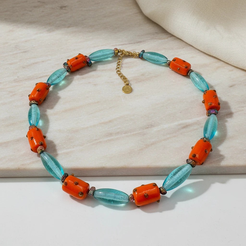 Handmade statement necklace with turquoise oval beads and orange barrel beads with textured details. Gold chain.