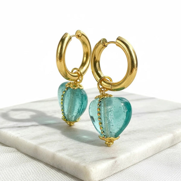 elephantina.gr gold hoop earrings with teal Murano glass heart charms and rhinestone accents on a marble base