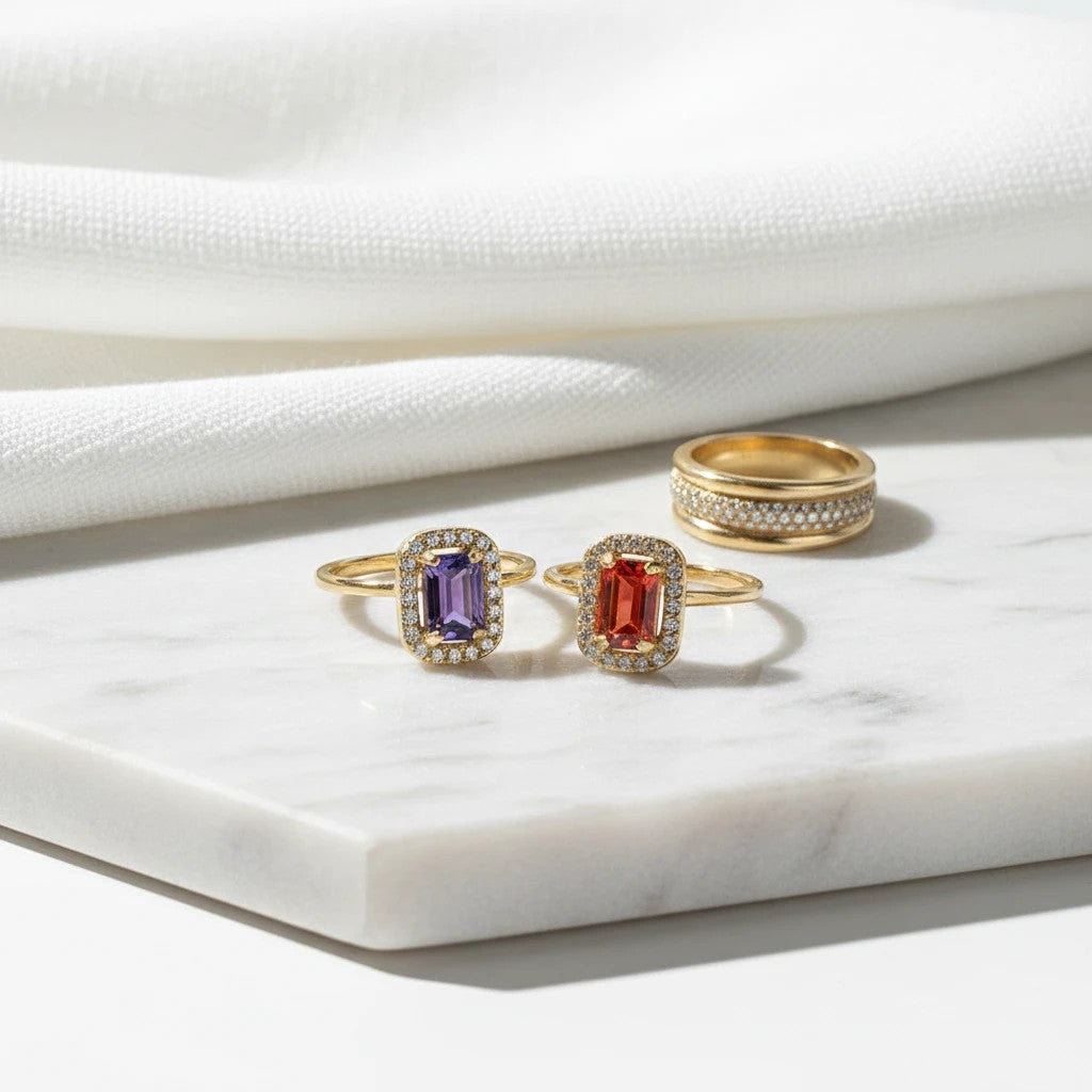 elephantina.gr rectangular gemstone rings with purple and orange stones, pavé crystal halos, and gold-tone bands.
