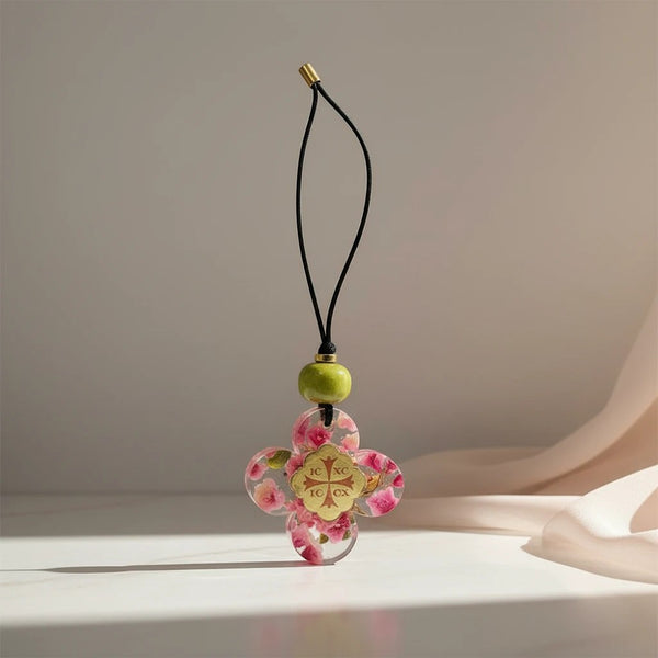 elephantina.gr floral resin cross charm with pink flowers and gold medallion on black cord with green bead.