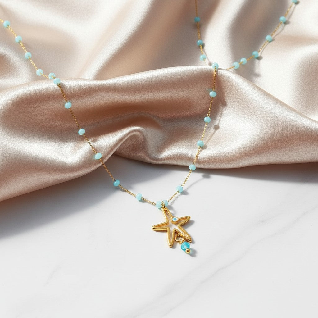 elephantina.gr gold necklace with blue crystal beads and a starfish or mermaid tail pendant with evil eye detail.