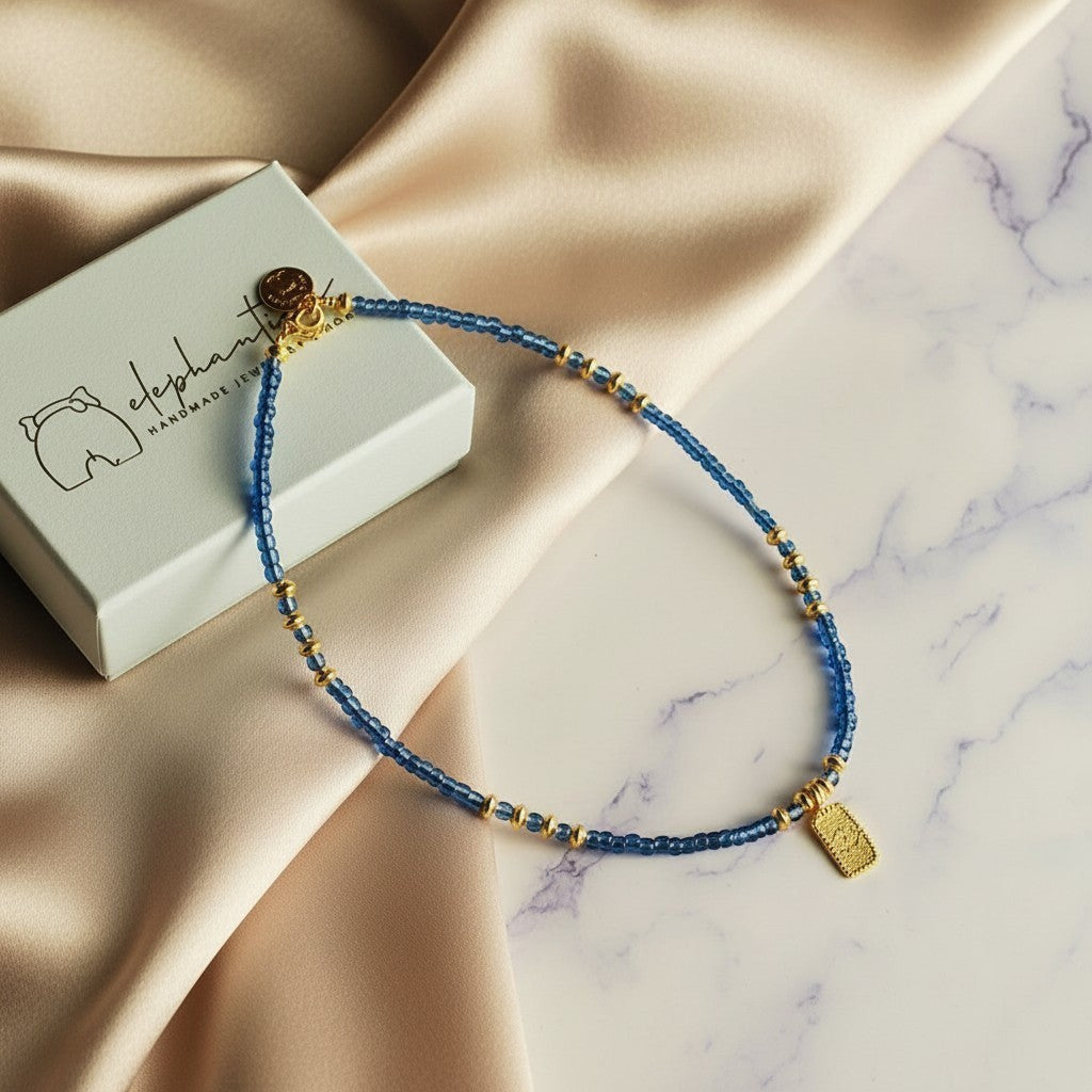elephantina.gr blue beaded necklace with gold accents and a hanging evil eye charm.