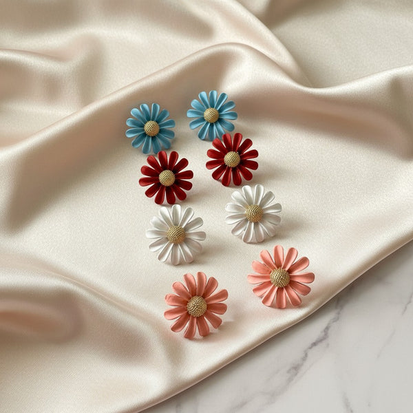 Elephantina.gr daisy stud earrings in blue, red, white, and coral. Enamel petals with gold-tone textured center.