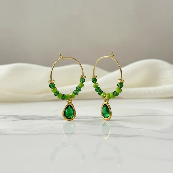 Gold hoop earrings with green beads and a teardrop emerald green crystal charm. elephantina.gr