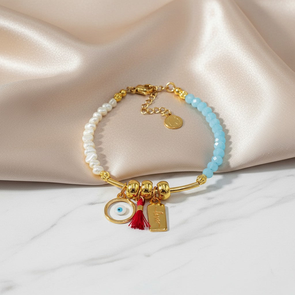 elephantina.gr handmade bracelet with pearls, blue beads, evil eye charm, red tassel, and 'love' tag. Gold tone.