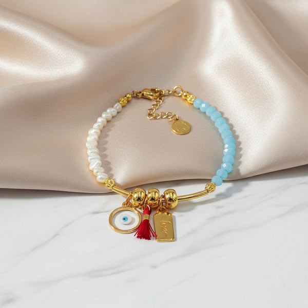 elephantina.gr handmade bracelet with pearls, blue beads, evil eye charm, red tassel, and 'love' tag. Gold tone.