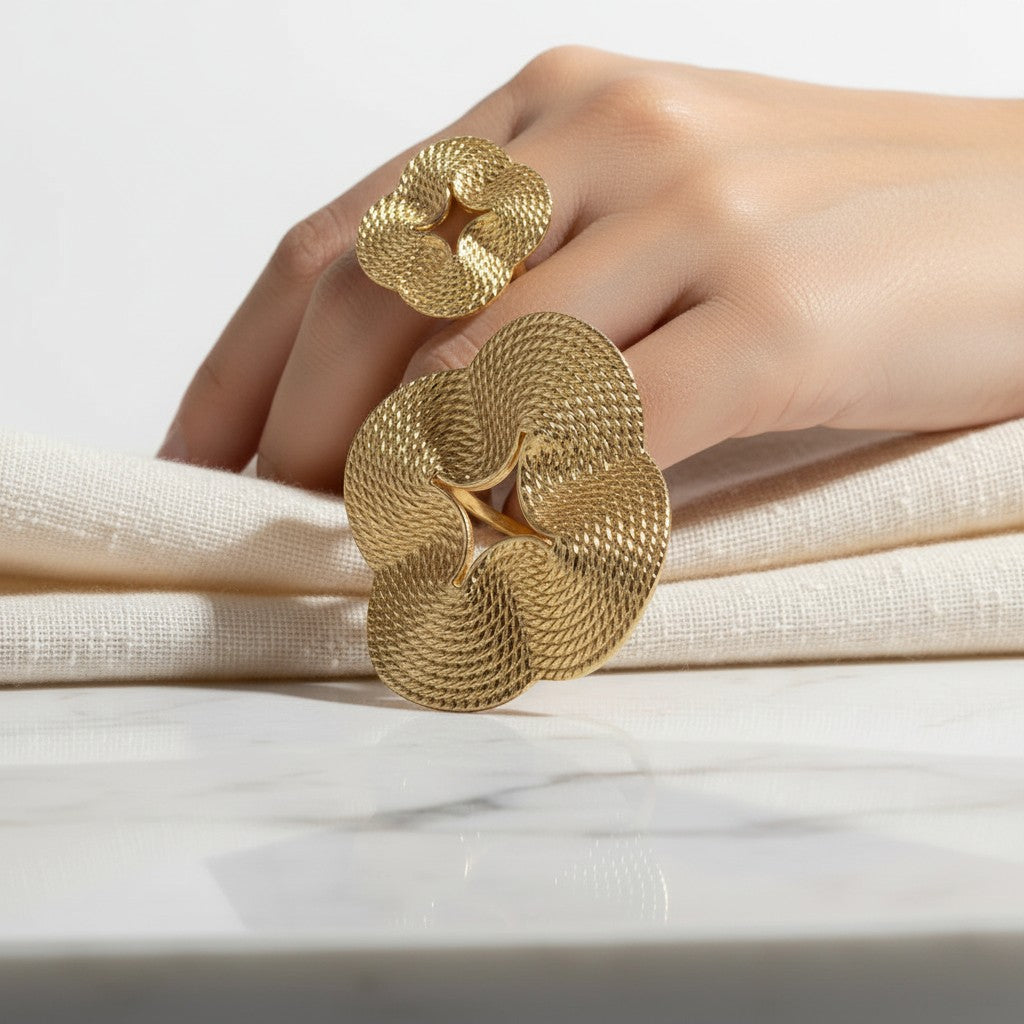 elephantina.gr gold-tone statement ring with a sculptural, textured floral design worn on a hand against white fabric.