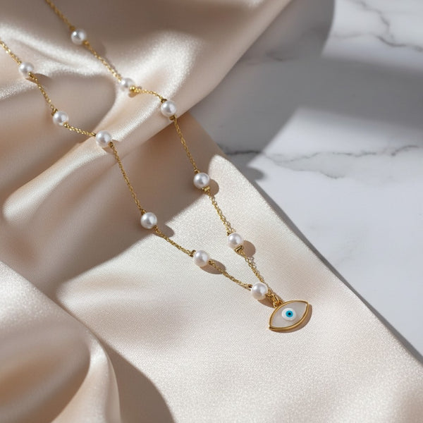 Gold stainless steel necklace with white pearls and a white evil eye charm with blue detail. Adjustable chain.