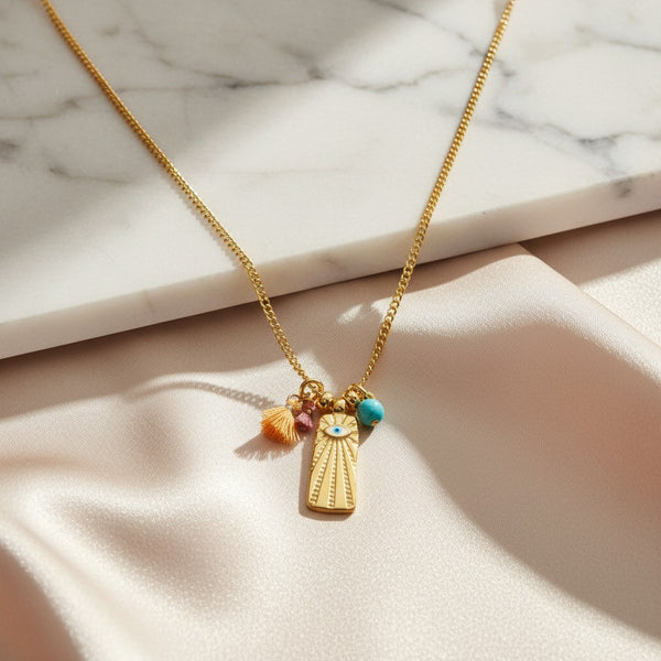 Gold plated stainless steel necklace with evil eye pendant, tassels, and turquoise bead. elephantina.gr
