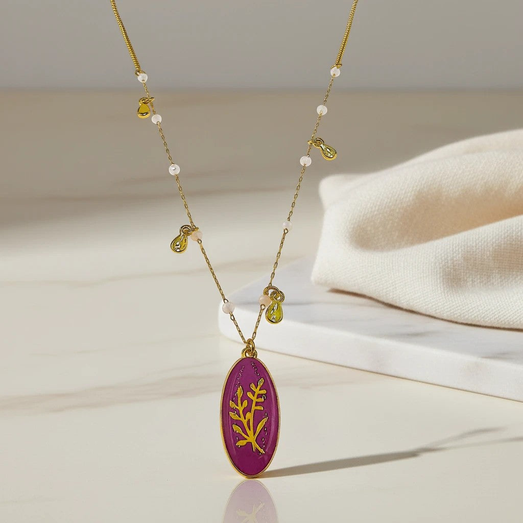 elephantina.gr gold chain necklace with white crystals and a magenta oval pendant with a gold branch design.
