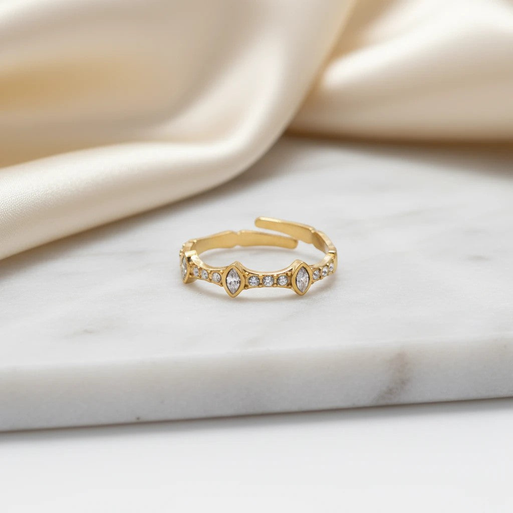 elephantina.gr gold-tone adjustable ring with marquise and round crystals on a marble surface with satin fabric.