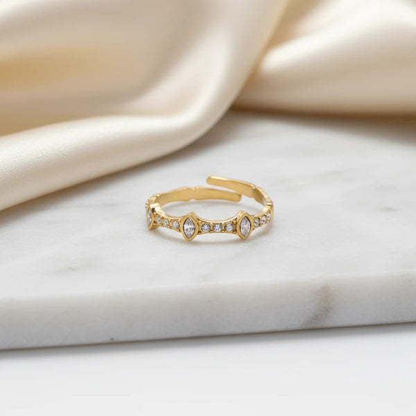 elephantina.gr gold-tone adjustable ring with marquise and round crystals on a marble surface with satin fabric.