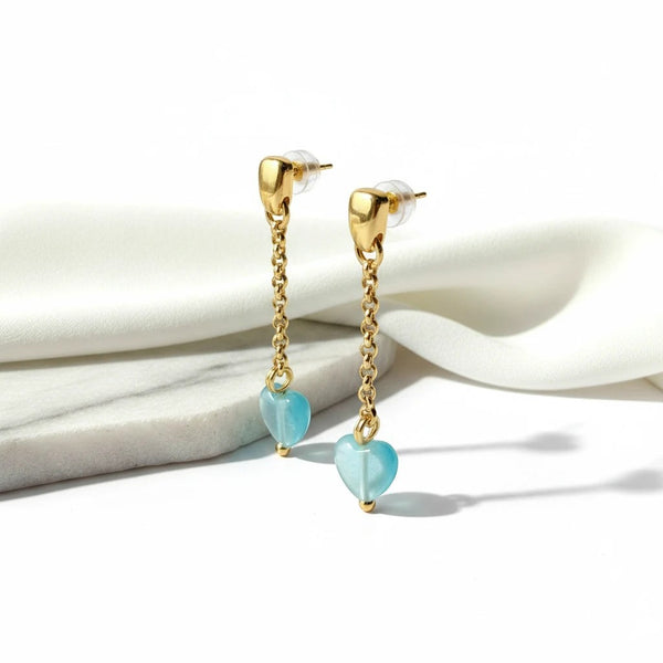 elephantina.gr baby blue cat's eye heart drop earrings with 24K gold-plated brass chain on a white marble base.