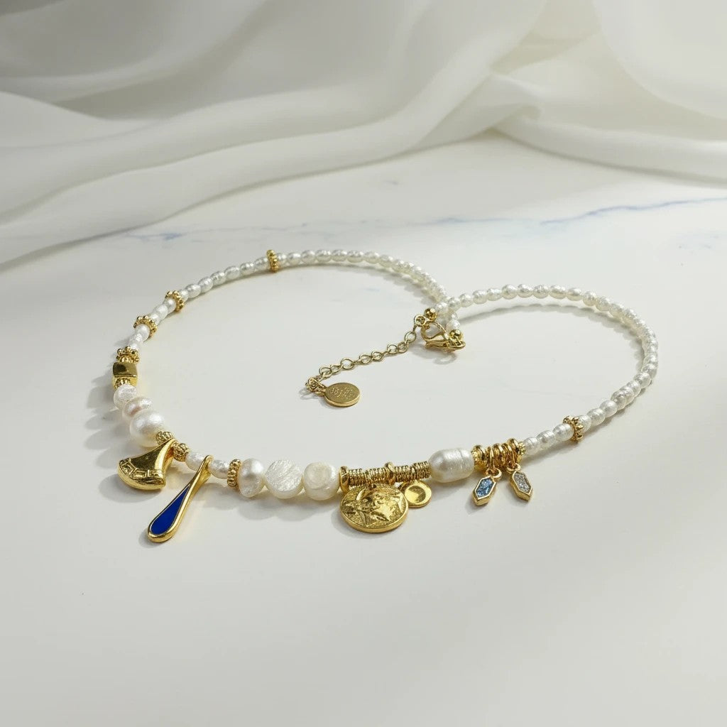 elephantina.gr pearl and gold charm necklace with navy drop, ancient Greek trumpet, and coin charms.