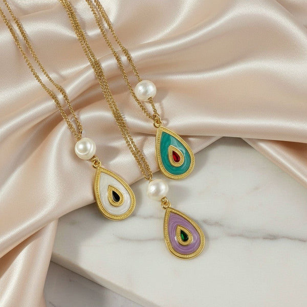 Elephantina.gr gold-plated teardrop pendant necklaces with pearl accents and colorful enamel. Features white, teal, and purple pendants.