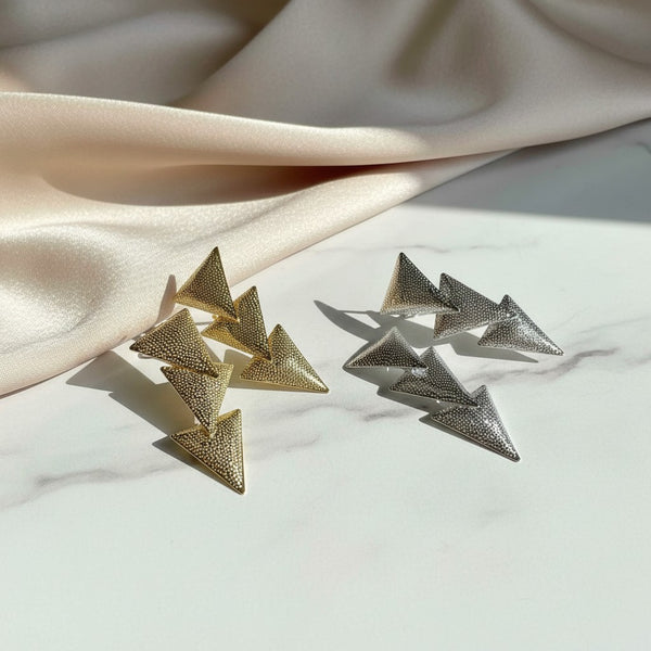 elephantina.gr gold and silver geometric triangle drop earrings with textured finish on a marble surface.