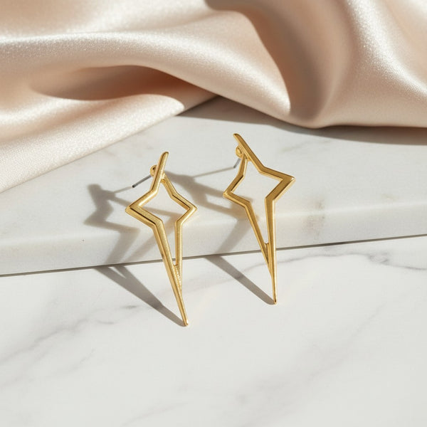 elephantina.gr gold-tone geometric starburst stud earrings with an open-frame design on a white marble surface.