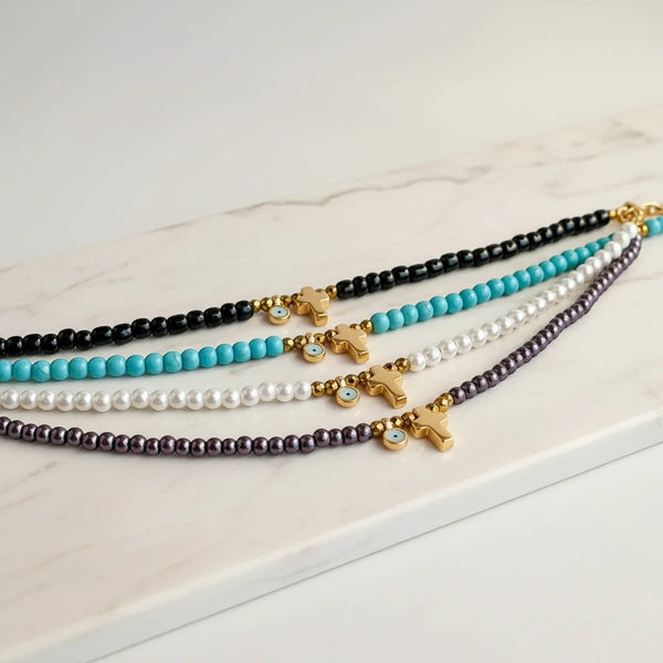 Elephantina.gr necklaces with gold crosses, blue evil eye charms, and pearls or beads in black, turquoise, white, and purple.